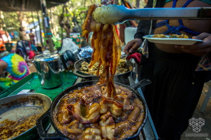 Bacon and sausage sizzling in a pan inside a makeshift kitchen.