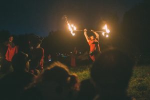 A fire spinner spins a staff with flaming prongs on either end.