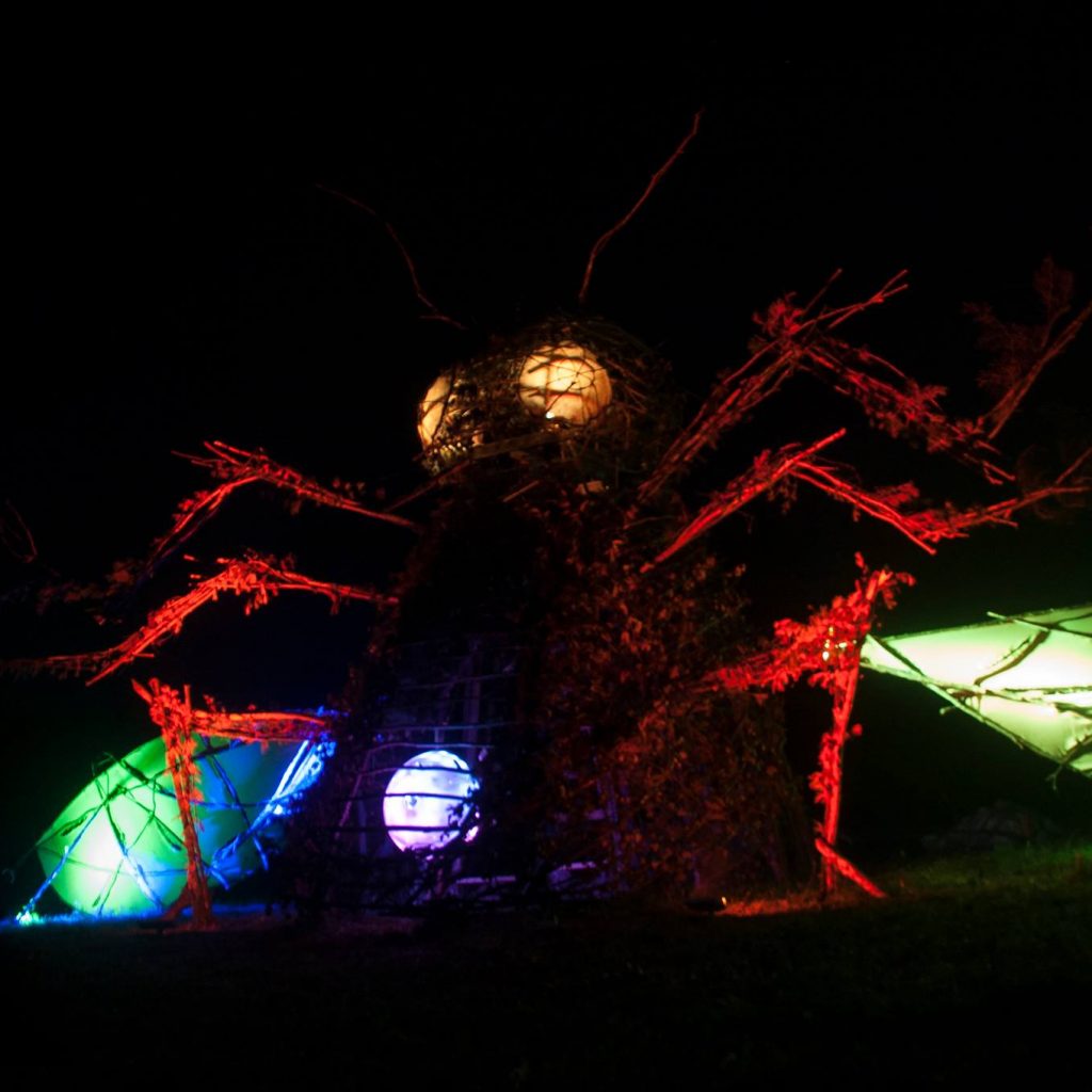 The 2012 bug at night. Its eyes and stomach-orb glow from within. Colored spotlights light the body and wings.